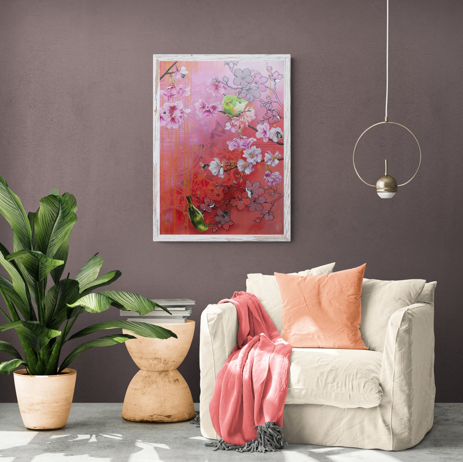 Painting 'Oh little beetle' from Cindy Sangen is hanging on a medium grey wall. The sunny room has a cream coloured chair with pink throw blanket and peach pillow. Next to it a plant and table with books.
